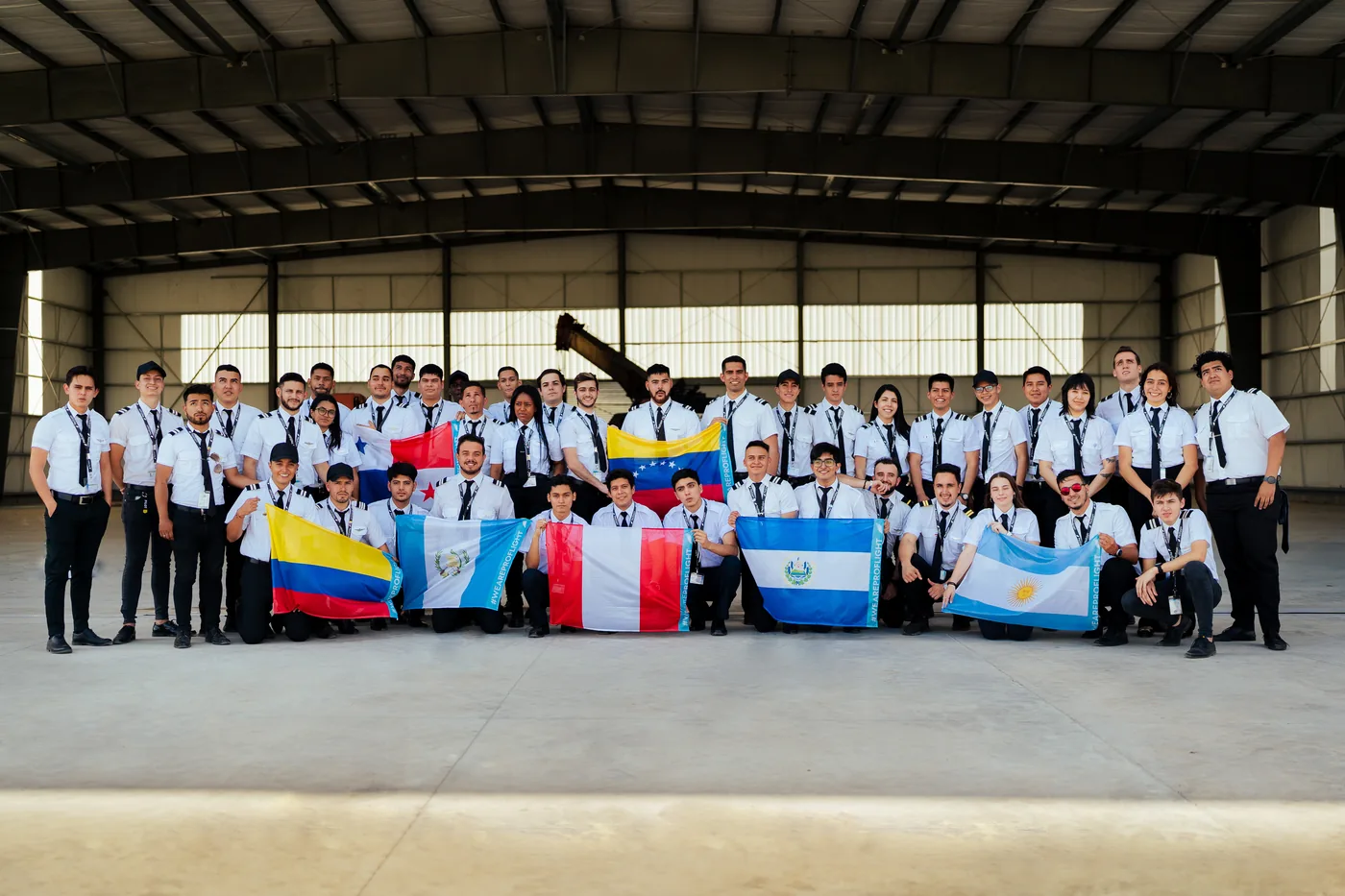 Estudiantes internacionales de ProFlight con las banderas de sus países en el hangar
